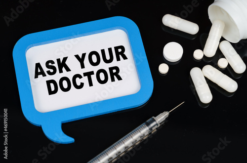 On a black surface, a syringe, pills and a blue frame with the inscription - ASK YOUR DOCTOR