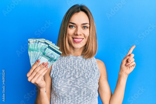 Young caucasian blonde woman holding 50 malaysia ringgit banknotes smiling happy pointing with hand and finger to the side photo