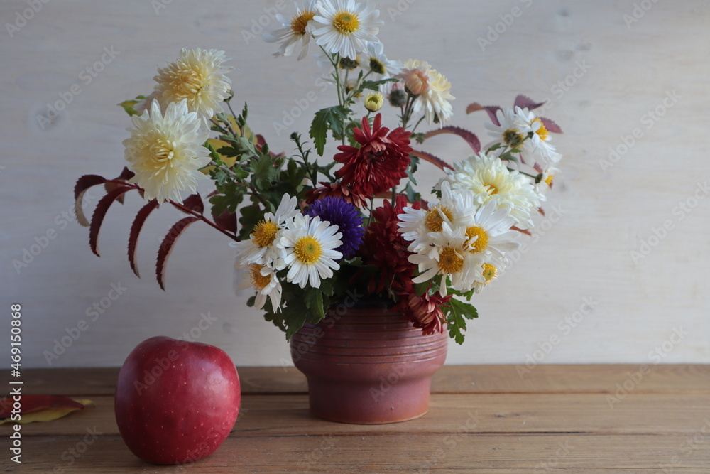Autumn bouquet of chrysanthemums, chamomiles in a vase and an apple on the table. Autumn bouquet of chrysanthemums, chamomiles in a vase and an apple on the table.