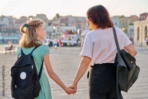 Mom and daughter child with backpack holding hands together, back view