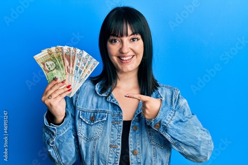 Young hispanic woman holding peruvian sol banknotes smiling happy pointing with hand and finger