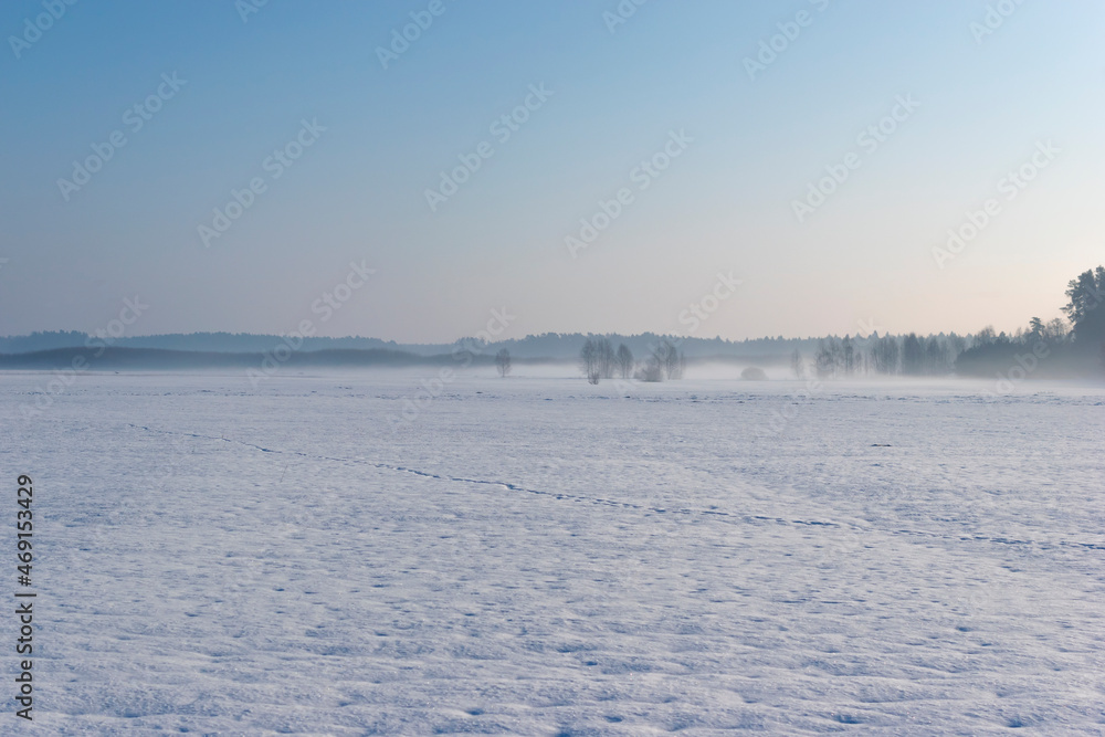 Landscape of winter in nature. Field covered the heavy snow with foot tracks on it near the forest in Europe.