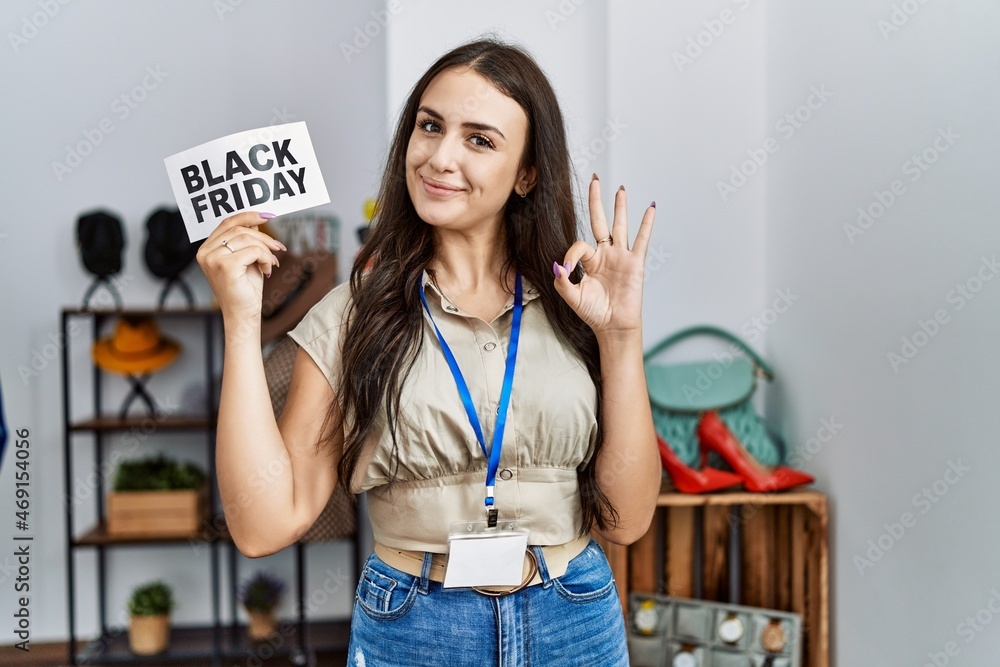 Young brunette woman holding black friday banner at retail shop doing ok sign with fingers, smiling friendly gesturing excellent symbol Young brunette woman holding black friday banner at retail shop doing ok sign with fingers, smiling friendly gesturing excellent symbol
