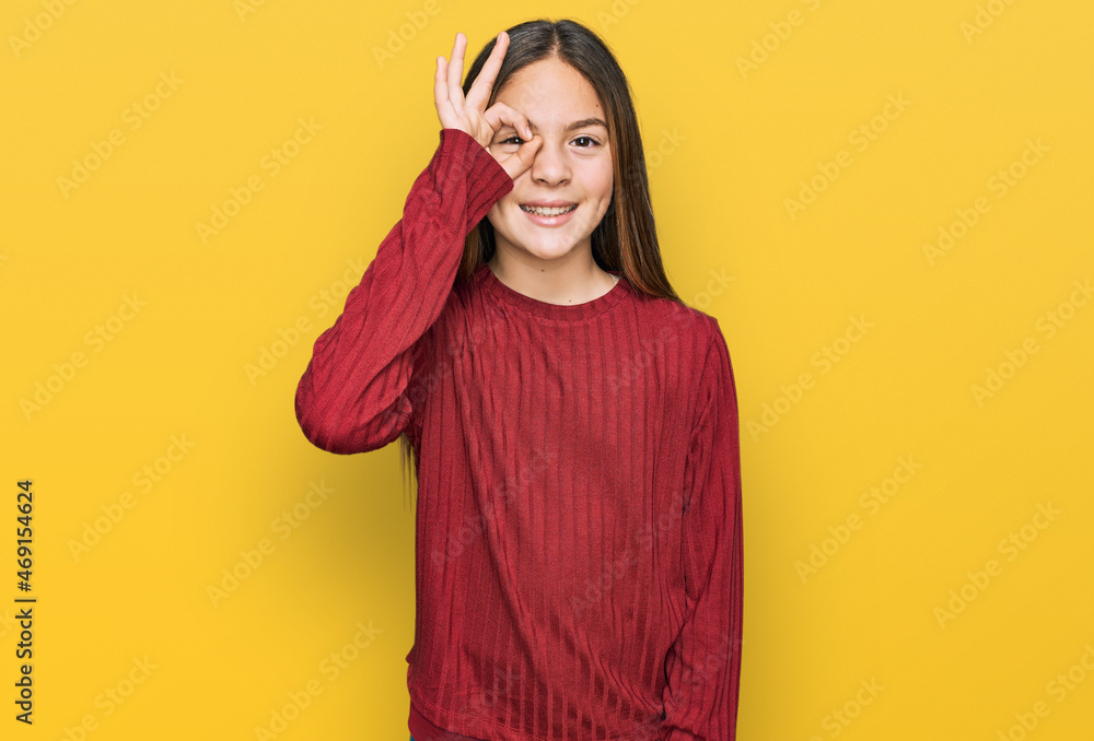 Beautiful brunette little girl wearing casual sweater doing ok gesture with hand smiling, eye looking through fingers with happy face. Beautiful brunette little girl wearing casual sweater doing ok gesture with hand smiling, eye looking through fingers with happy face.
