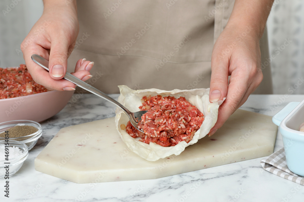 Woman preparing stuffed cabbage rolls at white marble table, closeup
