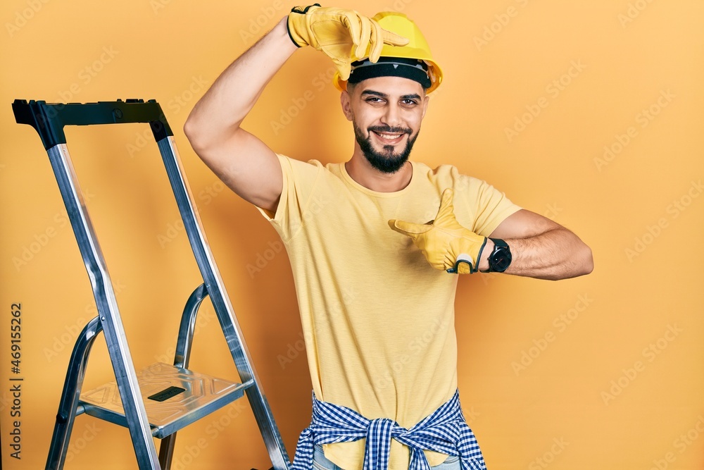 Handsome man with beard by construction stairs wearing hardhat smiling making frame with hands and fingers with happy face. creativity and photography concept. Handsome man with beard by construction stairs wearing hardhat smiling making frame with hands and fingers with happy face. creativity and photography concept.