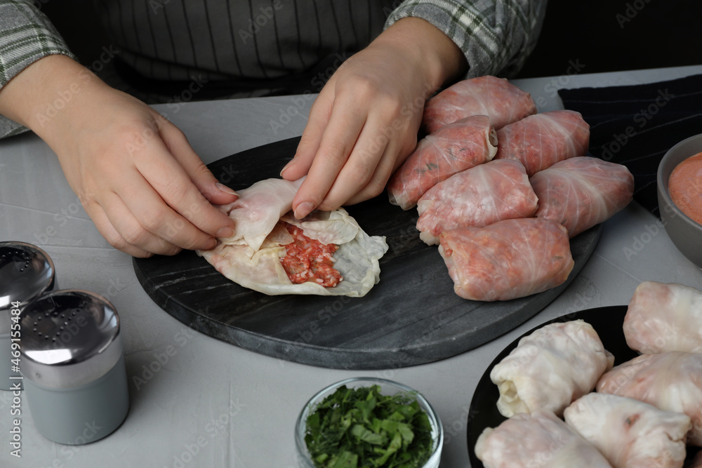 Woman making stuffed cabbage rolls at grey table, closeup