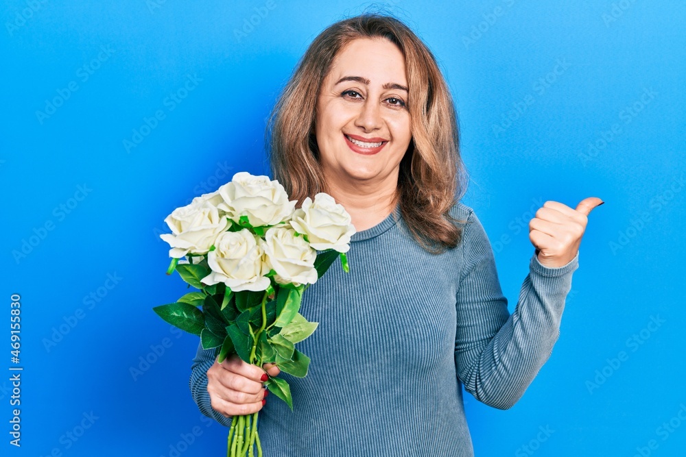Middle age caucasian woman holding flowers pointing thumb up to the side smiling happy with open mouth Middle age caucasian woman holding flowers pointing thumb up to the side smiling happy with open mouth