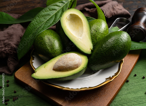 Avocado on a rustic wooden table in a white plate with gold border and leaves. Raw fruits are healthy green food.