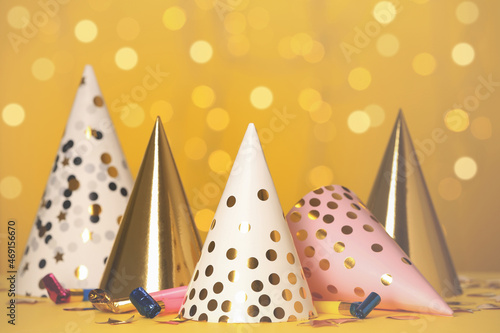 Party hats and festive items on table against yellow background with blurred lights
