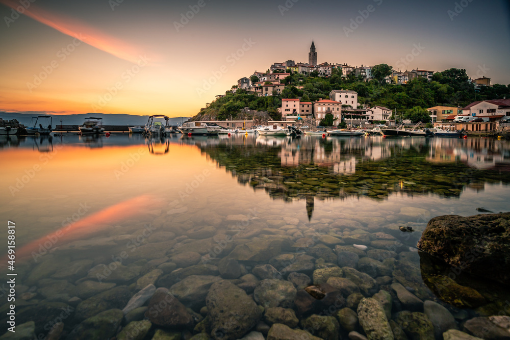 The historical place vrbnik in Croatsia on the island of Krk. In the sunrise directly on the sea, the port, the city is reflected on a rock in the water