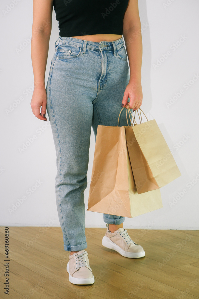 Naklejka premium Eco concept. An attractive girl in blue jeans and a black top holds brown craft paper bag in her hands. Ban on plastic bags. Cropped photo.