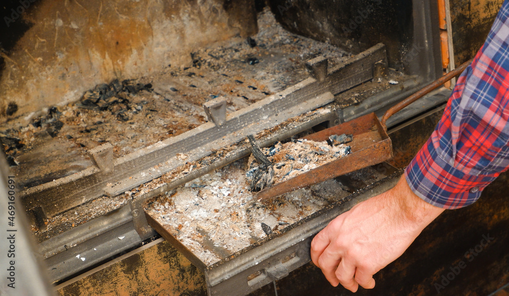 Ash removal from the fireplace. A man's hand in a plaid shirt holds a shovel with ash from the fireplace. A man cleans the fireplace. Ash removal from the fireplace. A man's hand in a plaid shirt holds a shovel with ash from the fireplace. A man cleans the fireplace.