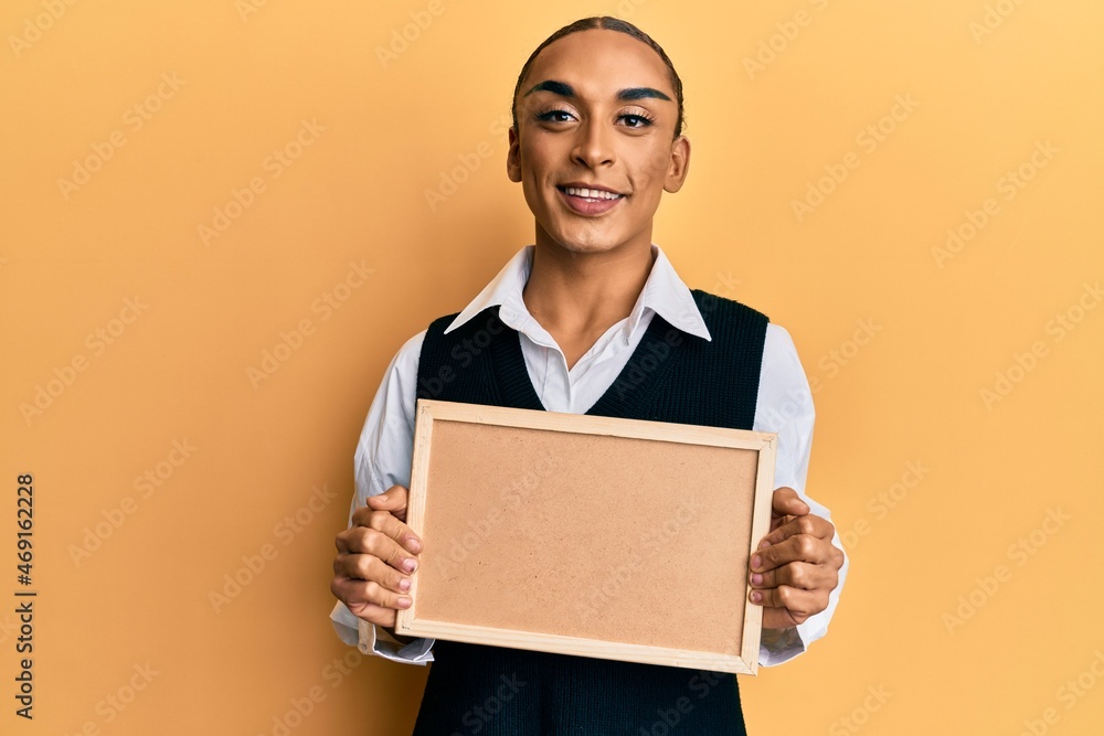 Hispanic man wearing make up and long hair holding empty corkboard smiling with a happy and cool smile on face. showing teeth. Hispanic man wearing make up and long hair holding empty corkboard smiling with a happy and cool smile on face. showing teeth.