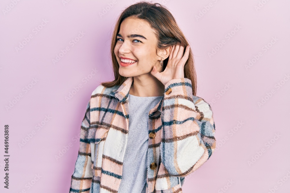 Young caucasian girl wearing casual clothes smiling with hand over ear listening an hearing to rumor or gossip. deafness concept. Young caucasian girl wearing casual clothes smiling with hand over ear listening an hearing to rumor or gossip. deafness concept.