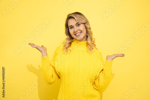 Young cute beautiful woman wearing yellow sweater standing over yellow isolated background with smiling face, pointing with hands to copy space for commersial sign. Positive emotion. Studio shot. © Татьяна Волкова