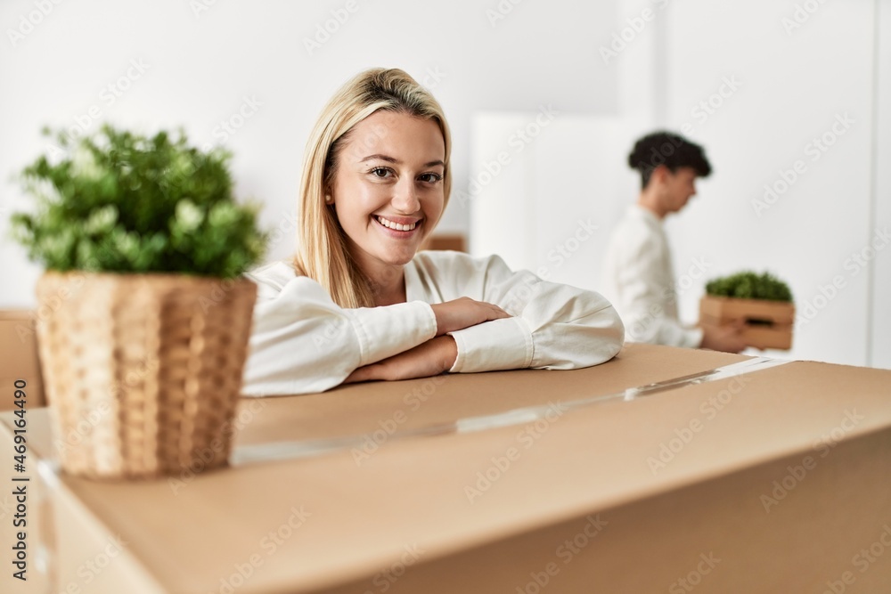 Young woman smiling happy leaning on cardboard at new home. Young woman smiling happy leaning on cardboard at new home.
