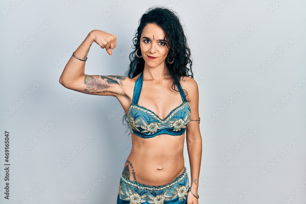 Young woman wearing bindi and traditional belly dance clothes strong person showing arm muscle, confident and proud of power Young woman wearing bindi and traditional belly dance clothes strong person showing arm muscle, confident and proud of power