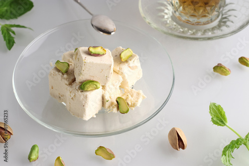 Halva with pistachios on a glass plate on a light background. Traditional oriental dessert Chekme. Natural vegan product. Turkish, Arab and Jewish national sweets