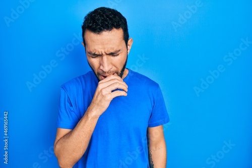 Hispanic man with beard wearing casual blue t shirt feeling unwell and coughing as symptom for cold or bronchitis. health care concept.