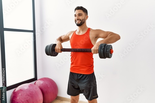 Young arab man smiling confident training with dumbbells at sport center