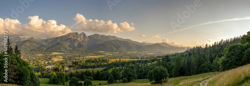 Panoramic landscape of a field with green grass trees and trail against giewont mountains covered with dramatic clouds located in Zakopane, Poland photo