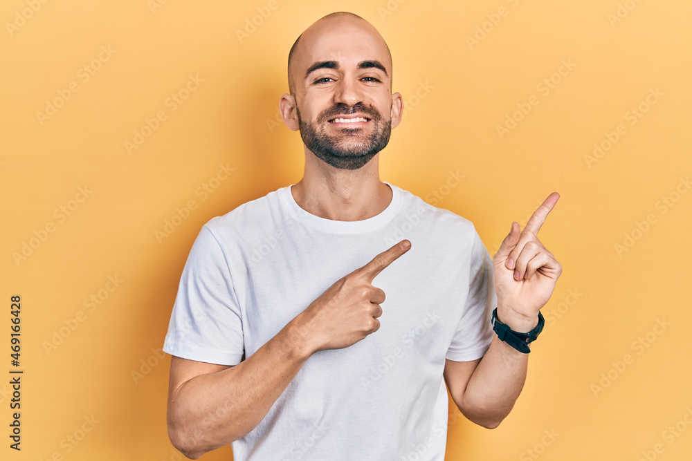 Young bald man wearing casual white t shirt smiling and looking at the camera pointing with two hands and fingers to the side. Young bald man wearing casual white t shirt smiling and looking at the camera pointing with two hands and fingers to the side.