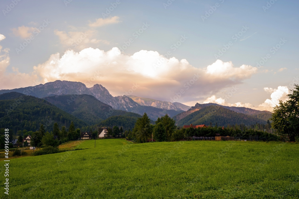 Fototapeta premium Wide angle view of a green field meadow in a countryside against giewont mountain in tatras during sunrise sunset located in Zakopane, Poland