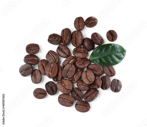Pile of roasted coffee beans with fresh leaf on white background, top view