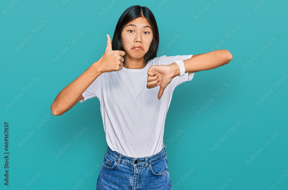 Beautiful young asian woman wearing casual white t shirt doing thumbs up and down, disagreement and agreement expression. crazy conflict Beautiful young asian woman wearing casual white t shirt doing thumbs up and down, disagreement and agreement expression. crazy conflict