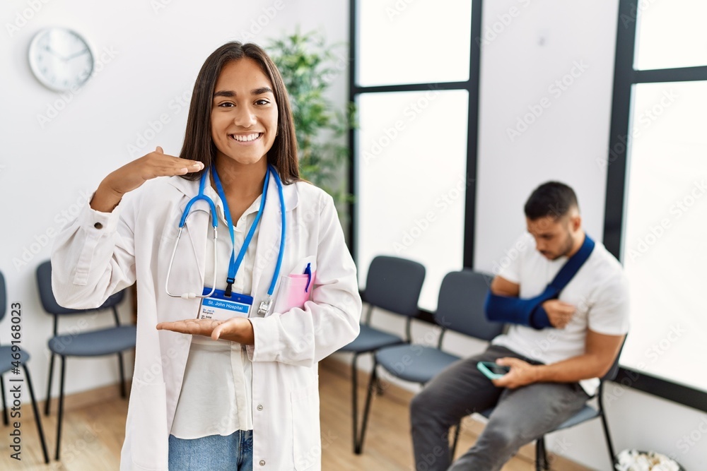 Young asian doctor woman at waiting room with a man with a broken arm gesturing with hands showing big and large size sign, measure symbol. smiling looking at the camera. measuring concept. Young asian doctor woman at waiting room with a man with a broken arm gesturing with hands showing big and large size sign, measure symbol. smiling looking at the camera. measuring concept.