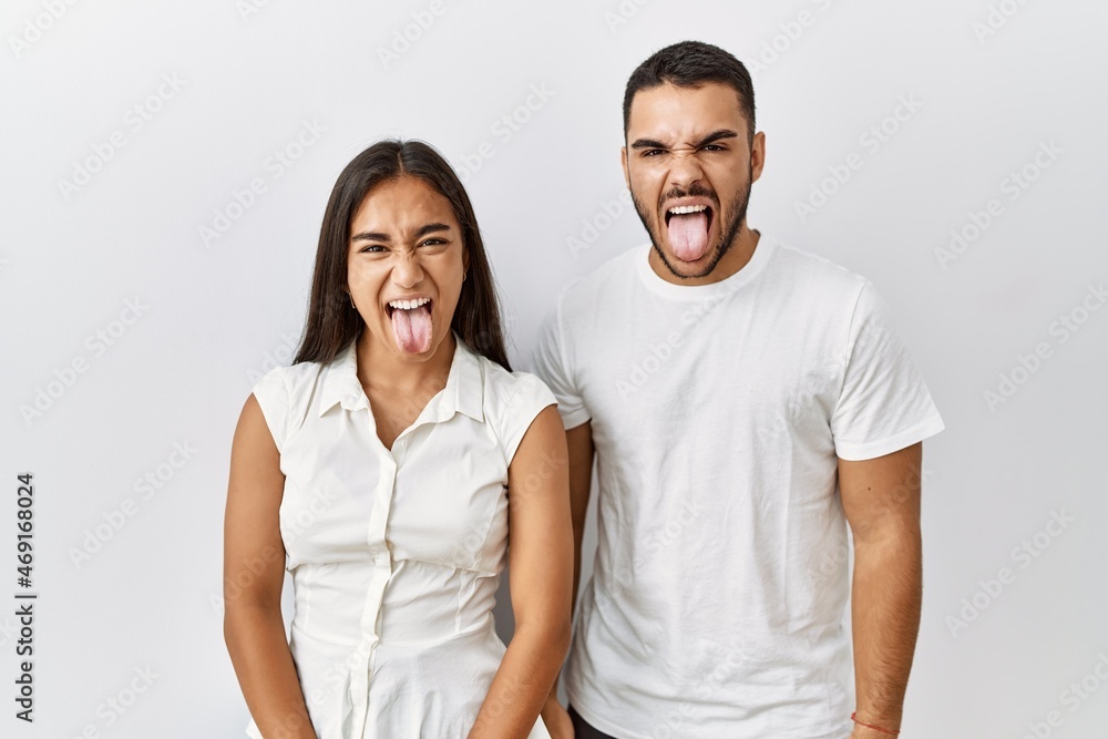 Young interracial couple standing together in love over isolated background sticking tongue out happy with funny expression. emotion concept. Young interracial couple standing together in love over isolated background sticking tongue out happy with funny expression. emotion concept.