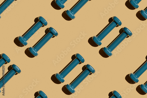 Two blue fitness dumbbells on a beige background lie parallel, pattern, top view, close-up. © Aleksandr Uglov