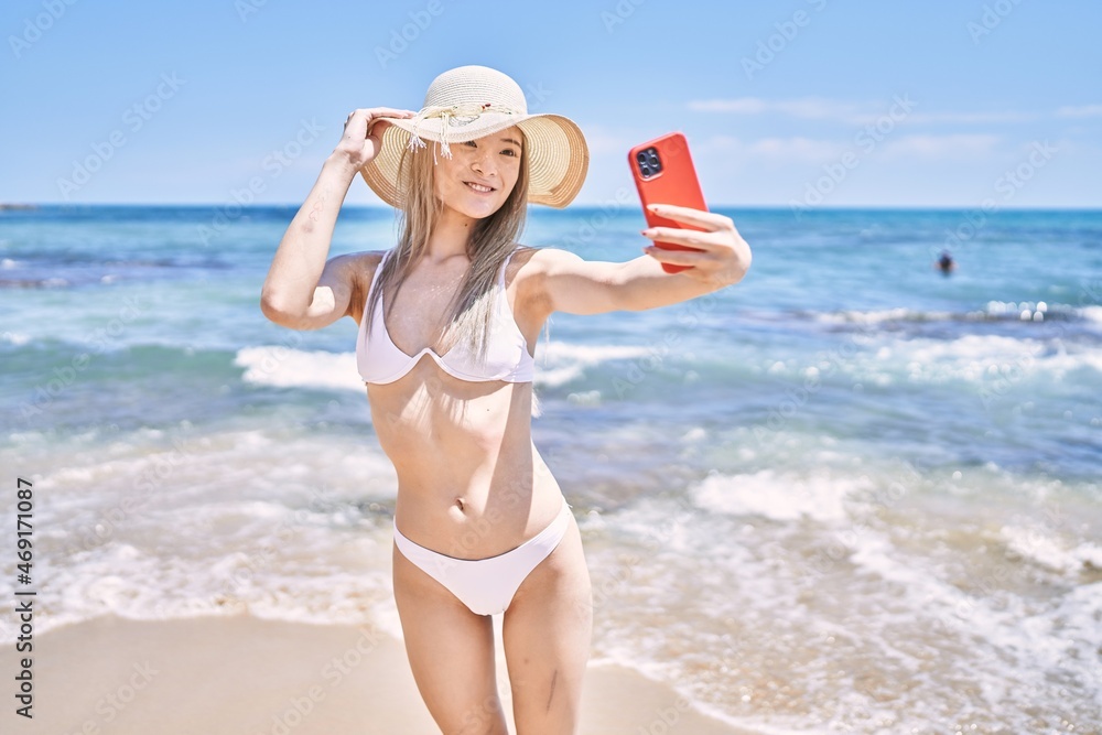 Young chinese girl wearing bikini make selfie by the smartphone at the beach.