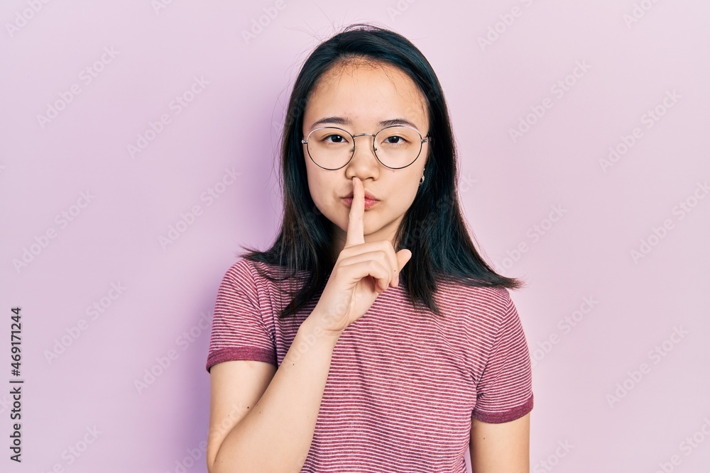Young chinese girl wearing casual clothes and glasses asking to be quiet with finger on lips. silence and secret concept. Young chinese girl wearing casual clothes and glasses asking to be quiet with finger on lips. silence and secret concept.