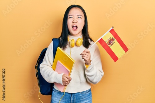 Young chinese girl exchange student holding spanish flag angry and mad screaming frustrated and furious  shouting with anger looking up.