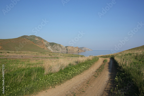 A road on the background of rocky mountains and the sea in the middle of blooming meadows