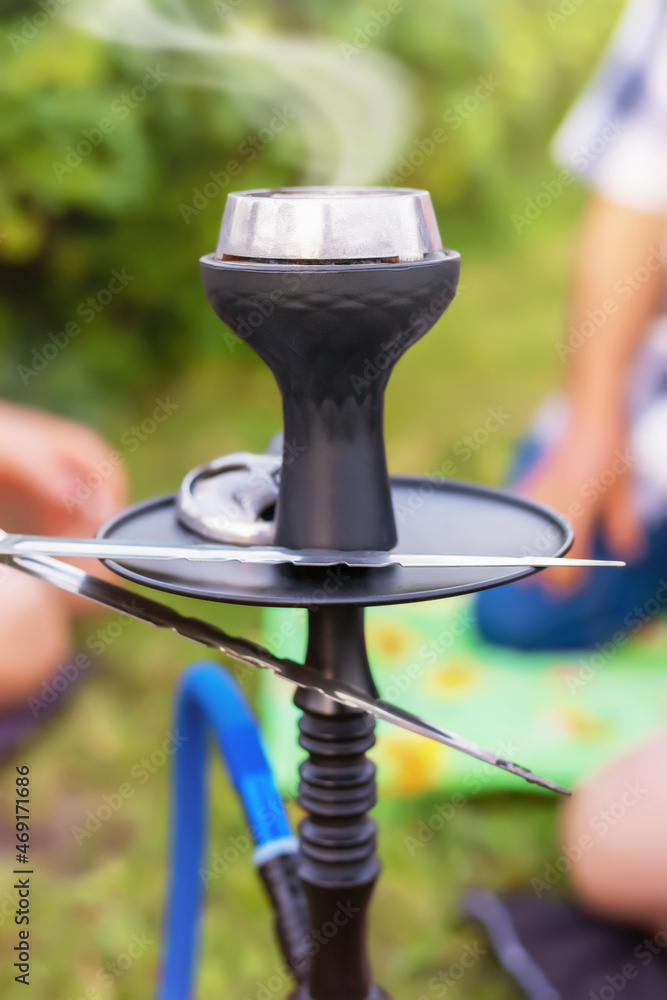 Obraz premium hookah with smoking coals, people are sitting around the hookah and smoking it outdoors