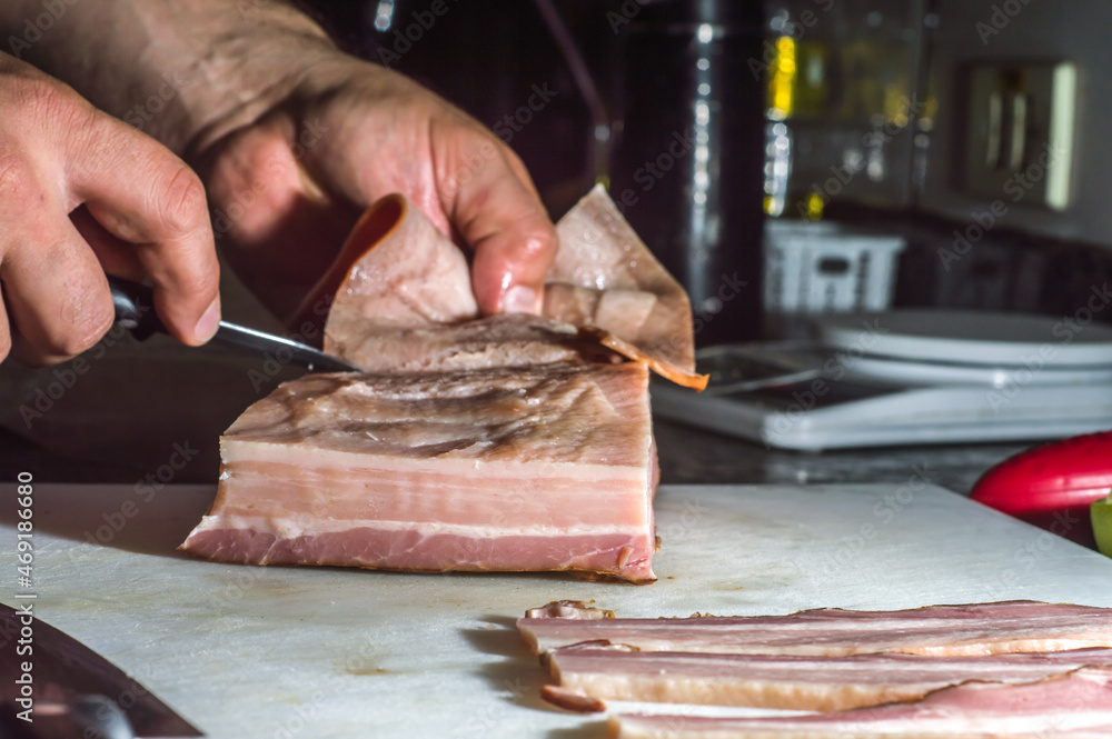 bacon on a white board with hands peeling skin with knife, dark background