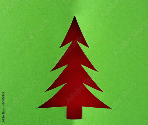 the outline of the Christmas tree cut out of green thick paper with a texture background red with shadows.
