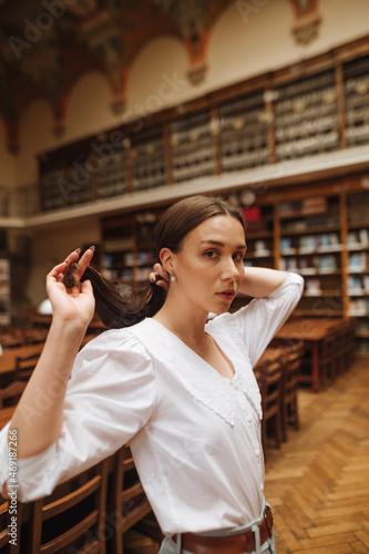 Beautiful female model in a white blouse posing for the camera in a public library.
