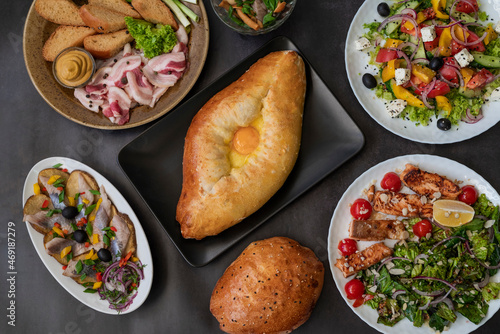 top view of khachapuri dish with cheese and egg in Adjarian with Caesar and Greek salads with potatoes and herring on the table