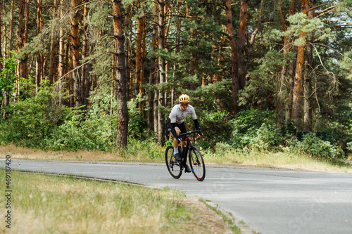 Handsome man in outfit goes cycling on a forest paved road outside the city. Outdoor cycling. © bodnarphoto