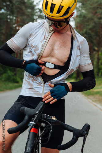 Professional cyclist in sports equipment measures heart rate monitor during training, sitting on a bicycle in the woods.