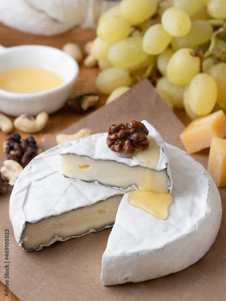 Brie cheese with nuts, honey and grapes on a a craft paper. Camembert with a cut piece, cheese with white mold
