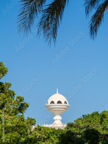 View to the Riyam Park monument dome through the palm leaves. Muscat, Oman.
