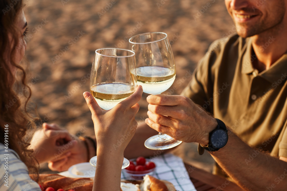 Close up of young couple drinking wine outdoors on beach while enjoying romantic date at sunset, copy space Close up of young couple drinking wine outdoors on beach while enjoying romantic date at sunset, copy space