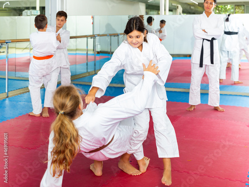 Focused school girls wearing white sports uniform practicing karate sparring in pair in gym