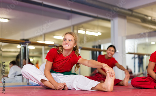 Kids in karate uniform sitting on floor with trainer and stretching their legs before group training.