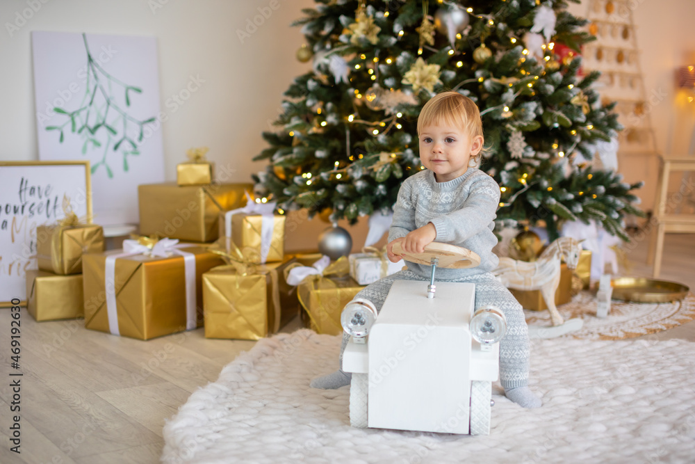 Adorable baby girl sitting near Christmas tree with festive lights and xmas gifts. Chrismas and New Year. Adorable baby girl sitting near Christmas tree with festive lights and xmas gifts. Chrismas and New Year.